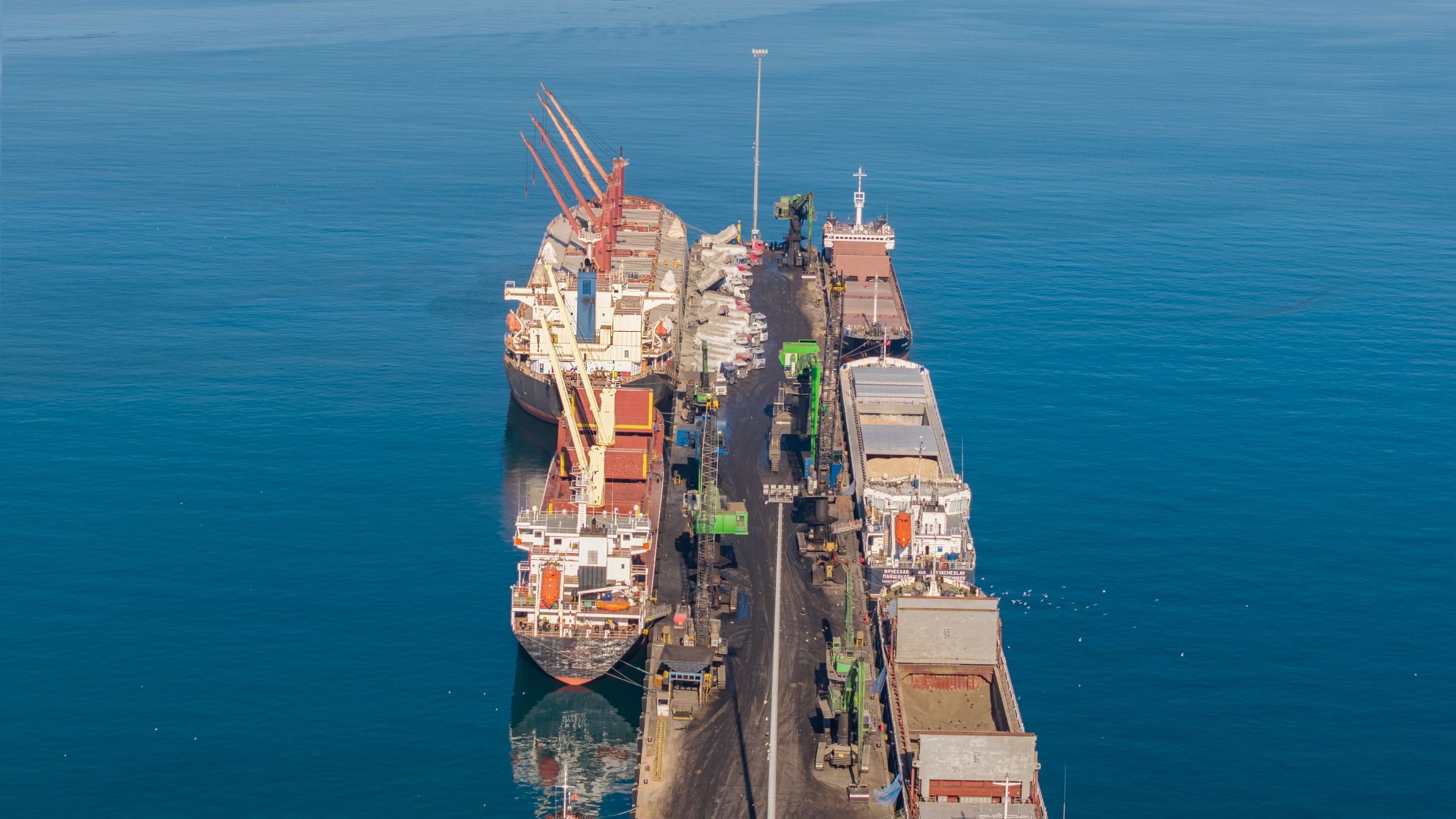 Aerial view of cargo ships docked at a busy industrial port with cranes loading and unloading goods
